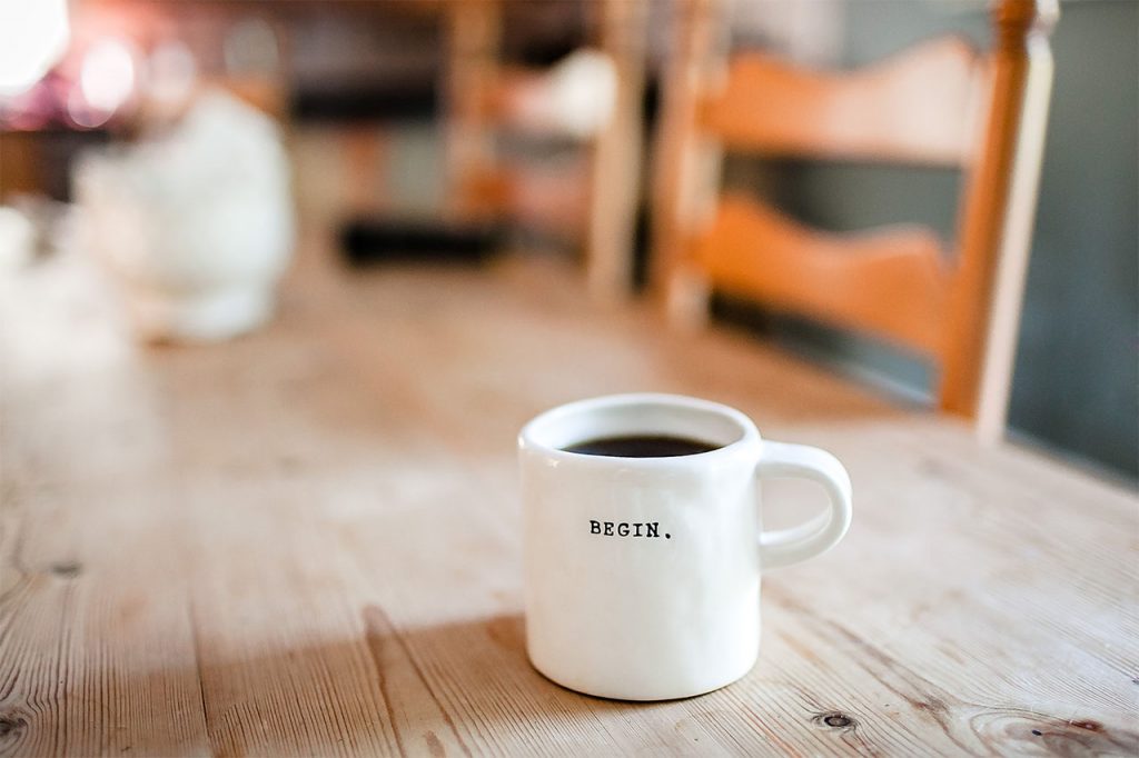 Eine Tasse Kaffe auf einem Holztisch, mit der Aufschrift: Beginn.