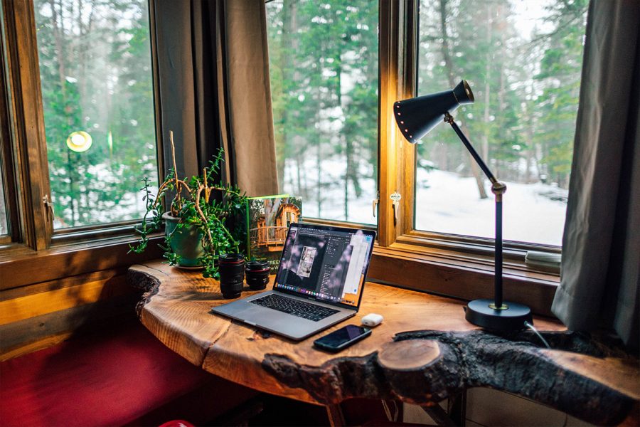 Ein Macbook auf einem Holztisch in einer gemütlichen Ecke mit warmem Licht und Pflanzen.