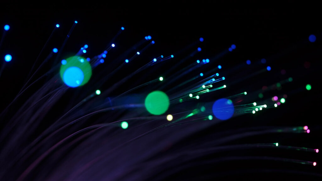 Leuchtende Glasfaserkabel mit bunten Lichtpunkten in Blau, Grün und Pink vor dunklem Hintergrund — veranschaulicht die Totalreflexion in der Glasfasertechnik (KI-generiert)